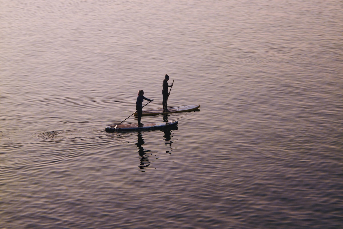 A couple of friends paddleboard across the water on Cape Cod in the summer.
