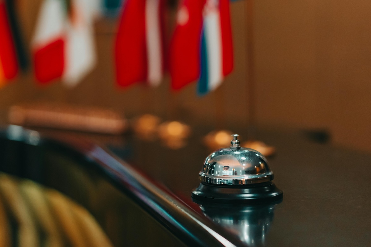 A bellhop bell on a desk in a European hotel, flags for various nation are seen behind the bell.