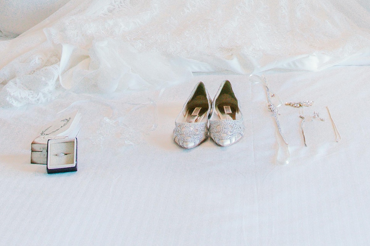 A bride's shoes and jewlery sit on a beautiful white bedspread. Her wedding dress is just out of sight above - she's being married on Cape Cod.