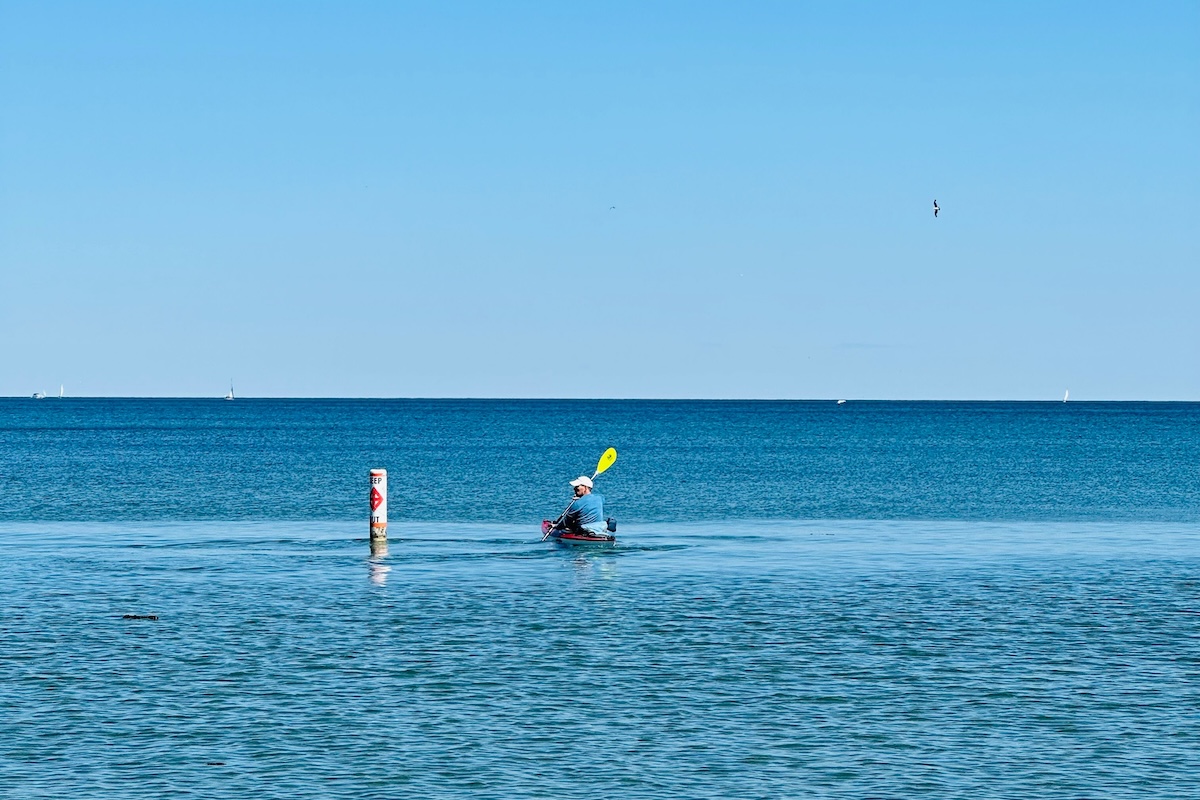 Solo kayaker paddling through calm blue waters under a clear sky.