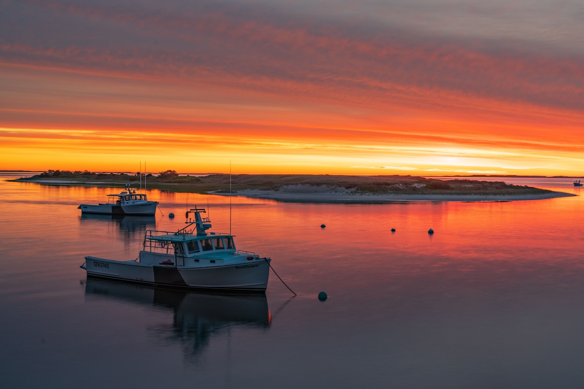 Peaceful sunrise over Chatham Harbor, Massachusetts with boats reflecting vivid colors.