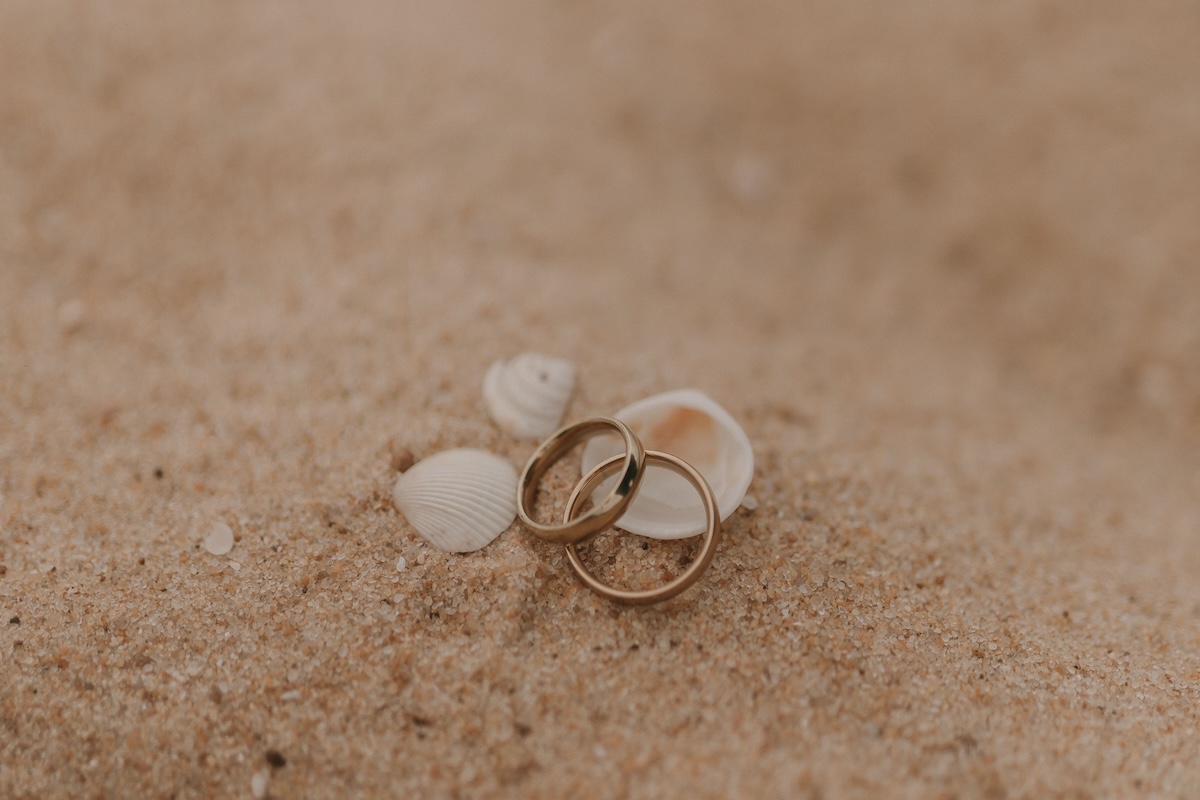 Gold wedding rings on a sandy beach with seashells, symbolizing love and romance.