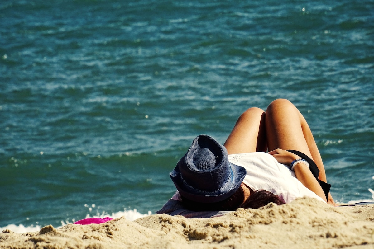 Woman in a hat relaxing on a sandy beach with a view of the ocean under the summer sun.