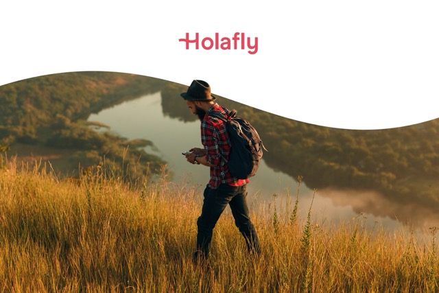 man walking in hills on phone with Holafly brand logo