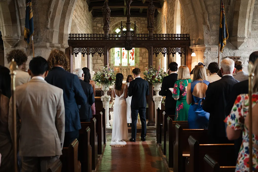 a view from the end of the aisle - bride and groom during ceremony with tall flower urns at the alter