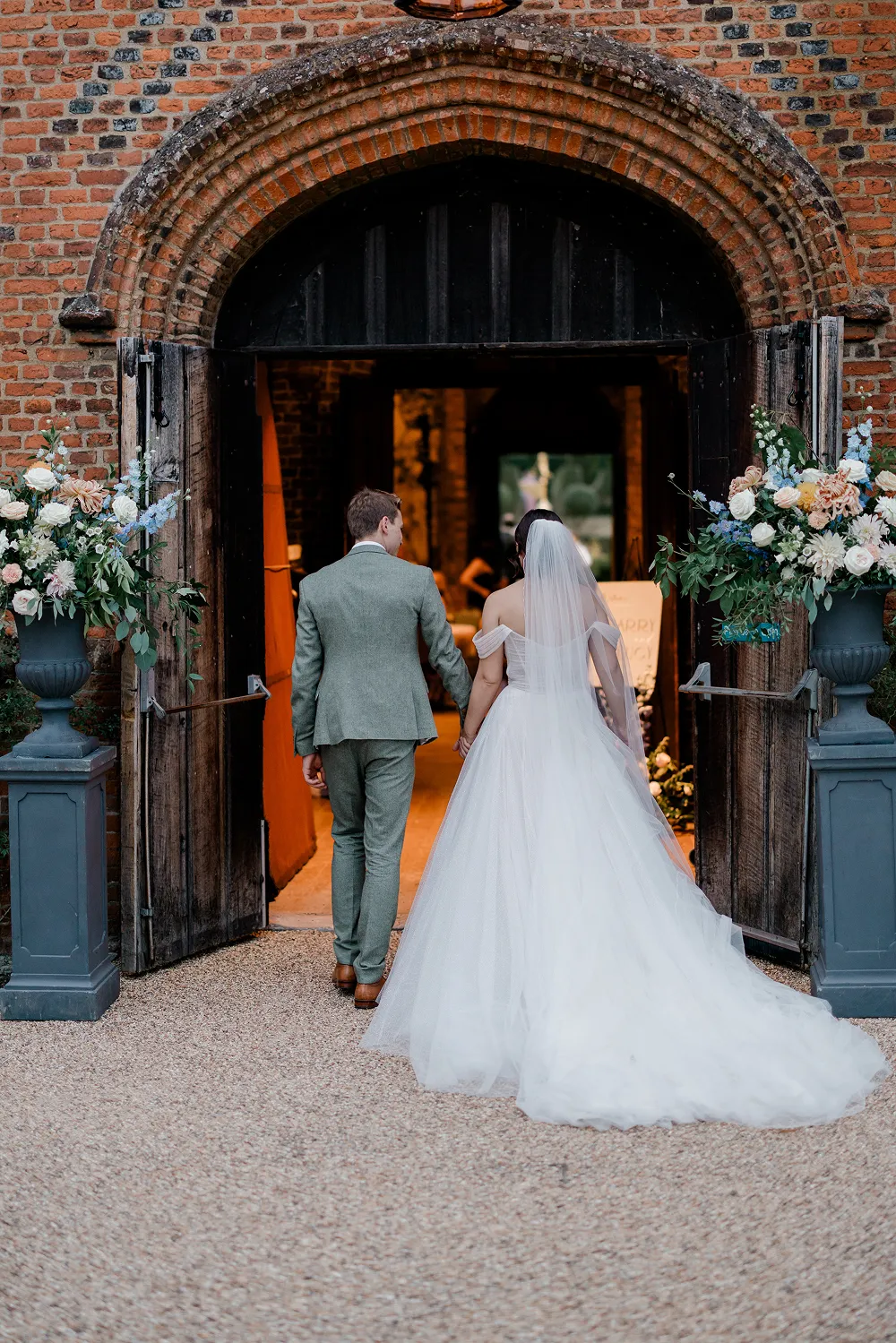 bride and groom walking into wedding venue with tall flower urns either side