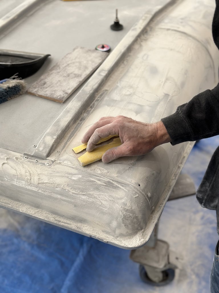 Hand-sanding body panel during paint preparation