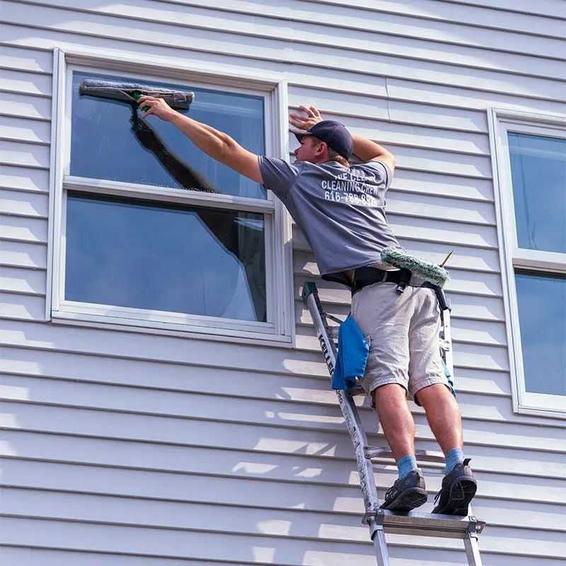 A window cleaning technician with Marine Clean Power Washing is cleaning windows using a ladder.