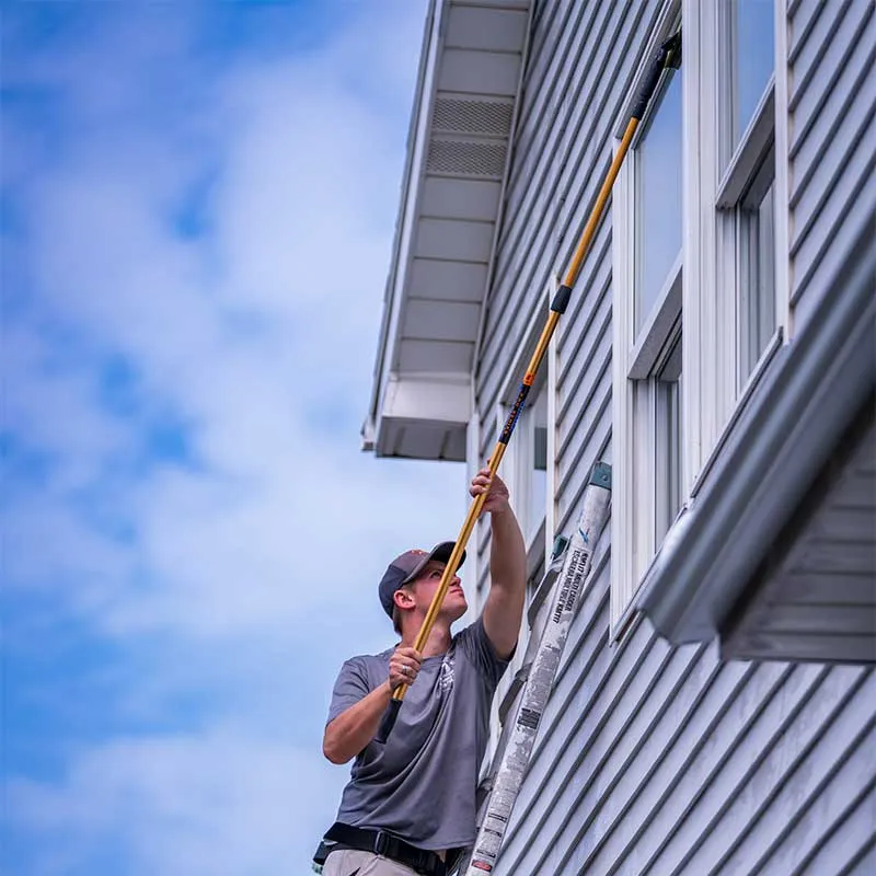 A window cleaning technician with Marine Clean Power Washing is cleaning windows using a ladder.