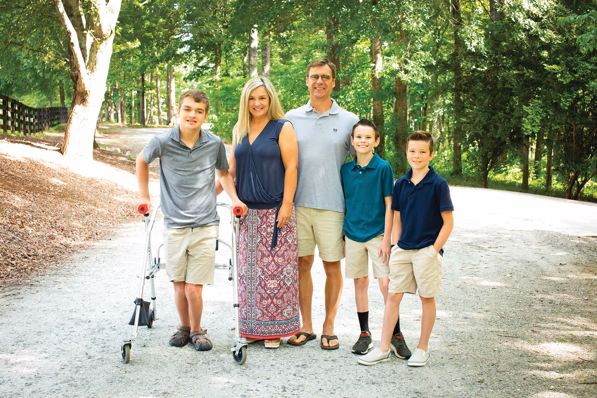 Family of five standing on a sunlit forest path, with one boy using a walker and others smiling.