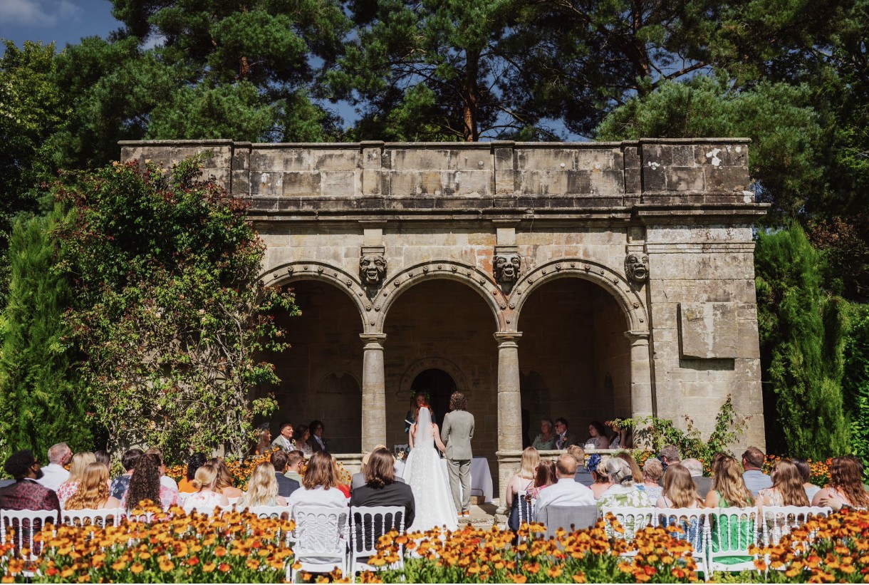Set in a walled gardens, chairs sit in front of an old Italian style Loggia while a musician plays to the side of the building. 
