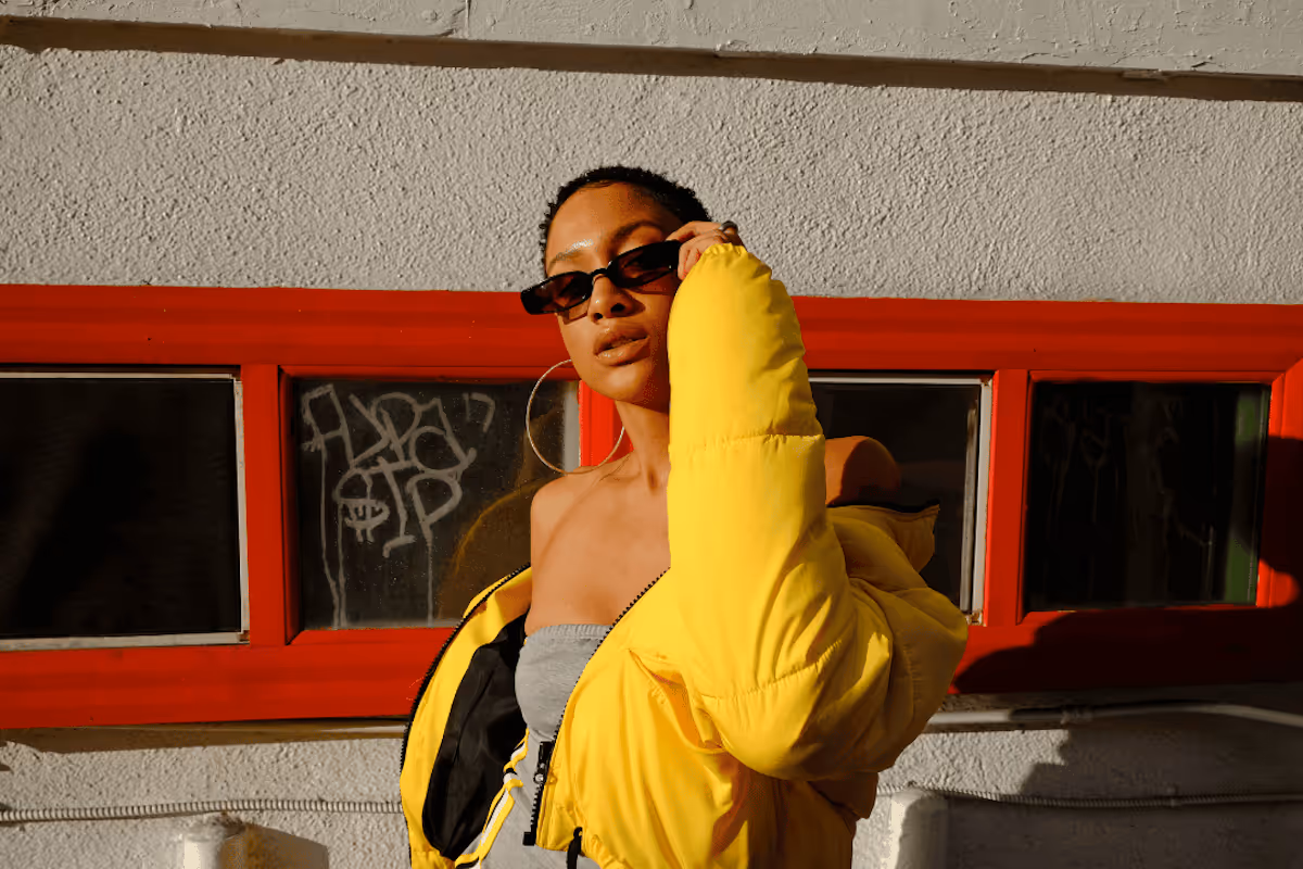 A fashionable woman wearing sunglasses and a yellow jacket outside.