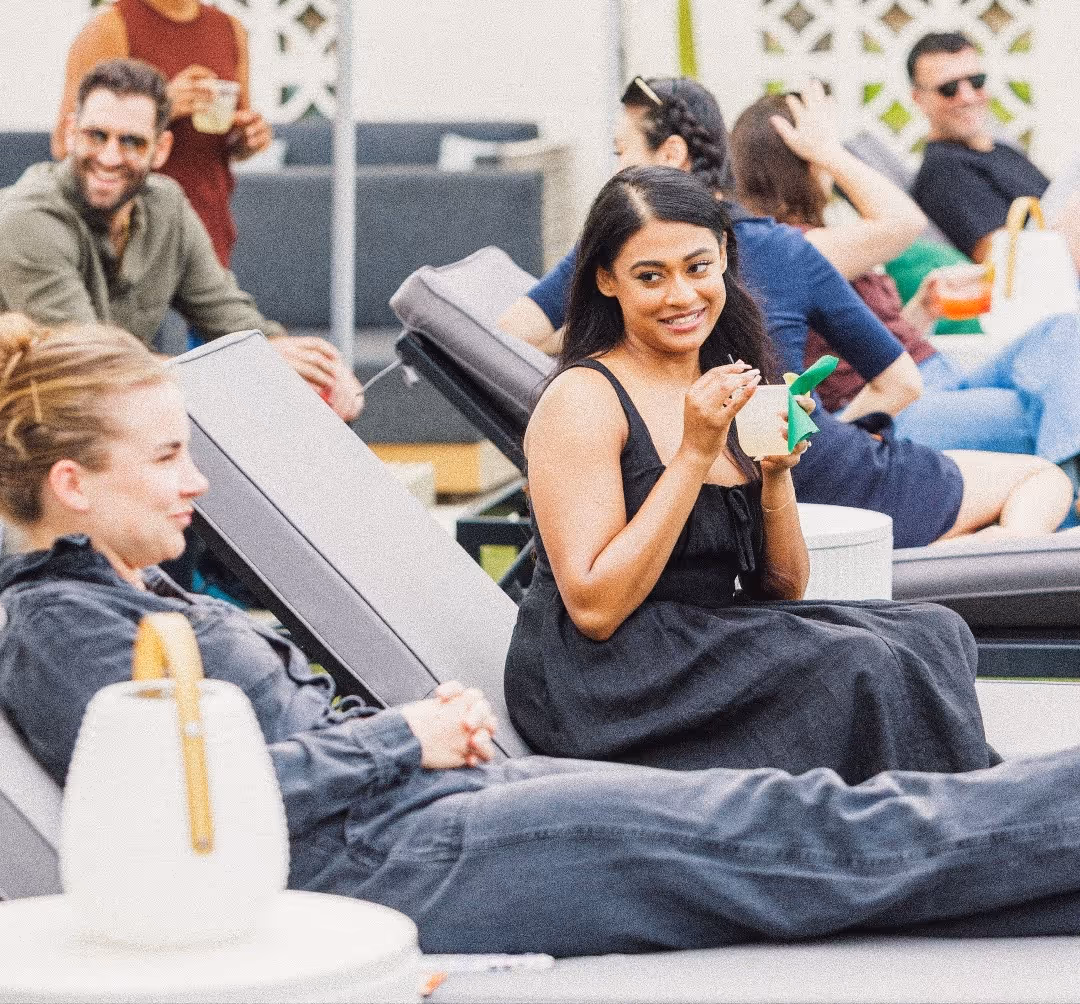 Group of people sitting and chatting on lounge chairs, one woman eating from a cup.