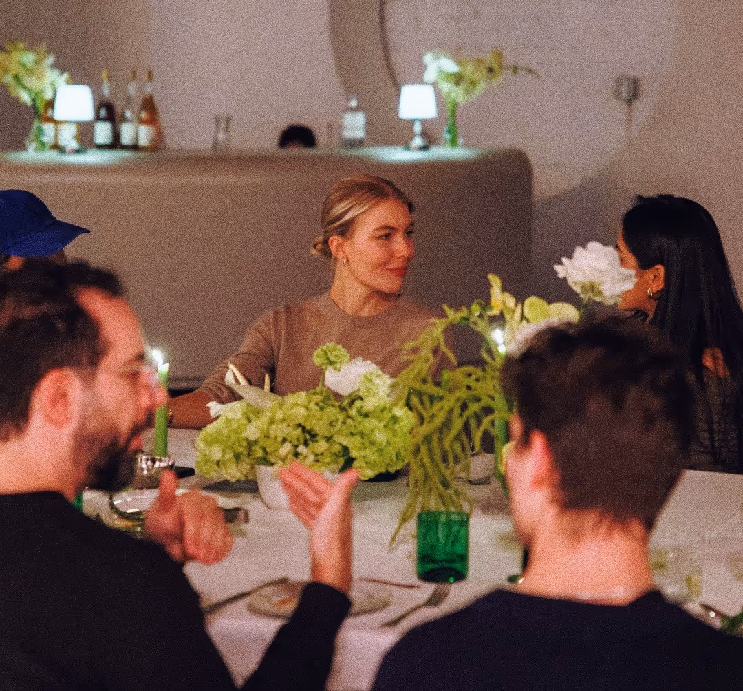Four people seated at a table with white tablecloth and green floral centerpiece, engaged in conversation.