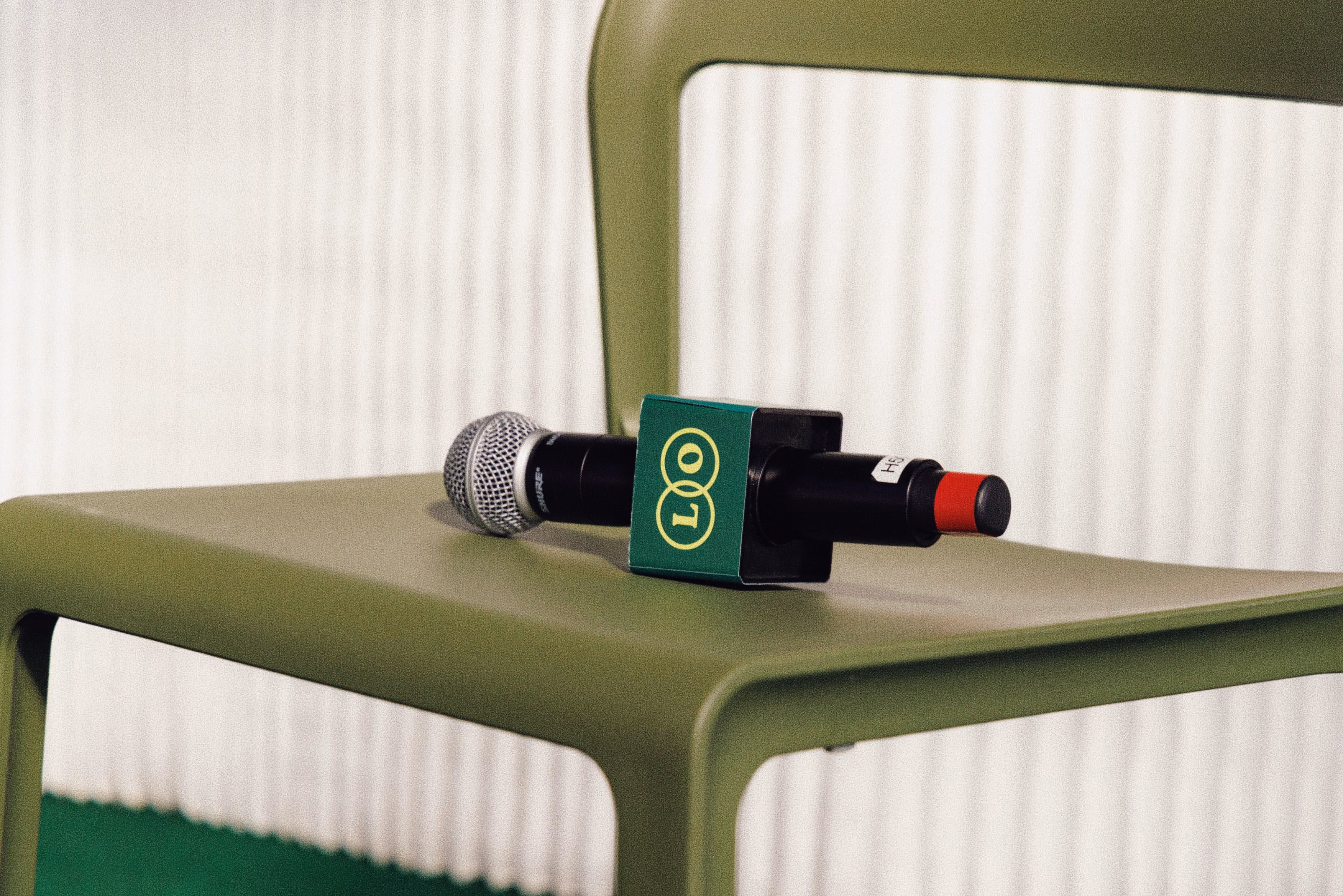 Microphone with a green LOO flag resting on an olive green chair with a textured white background.