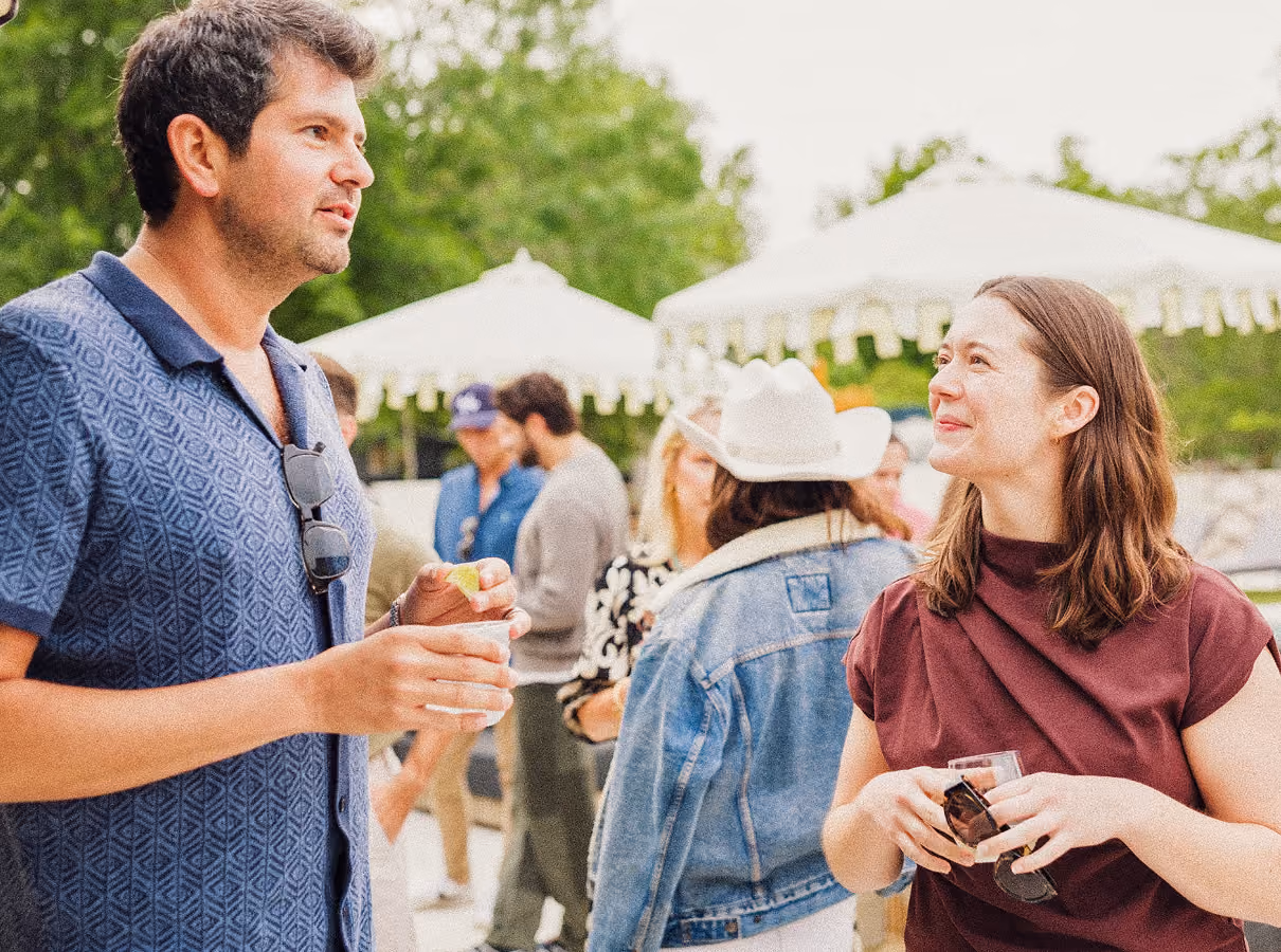 Man and woman chatting outdoors at a social event with others and white tents in background.