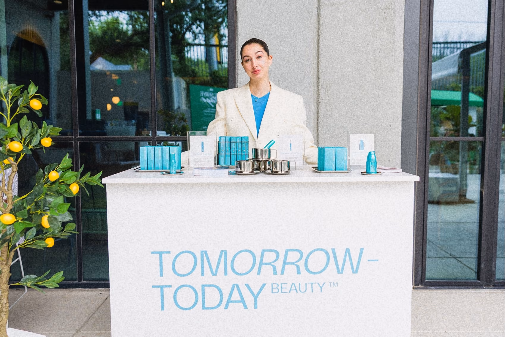 Woman behind a white counter displaying turquoise beauty products labeled Tomorrow-Today Beauty.