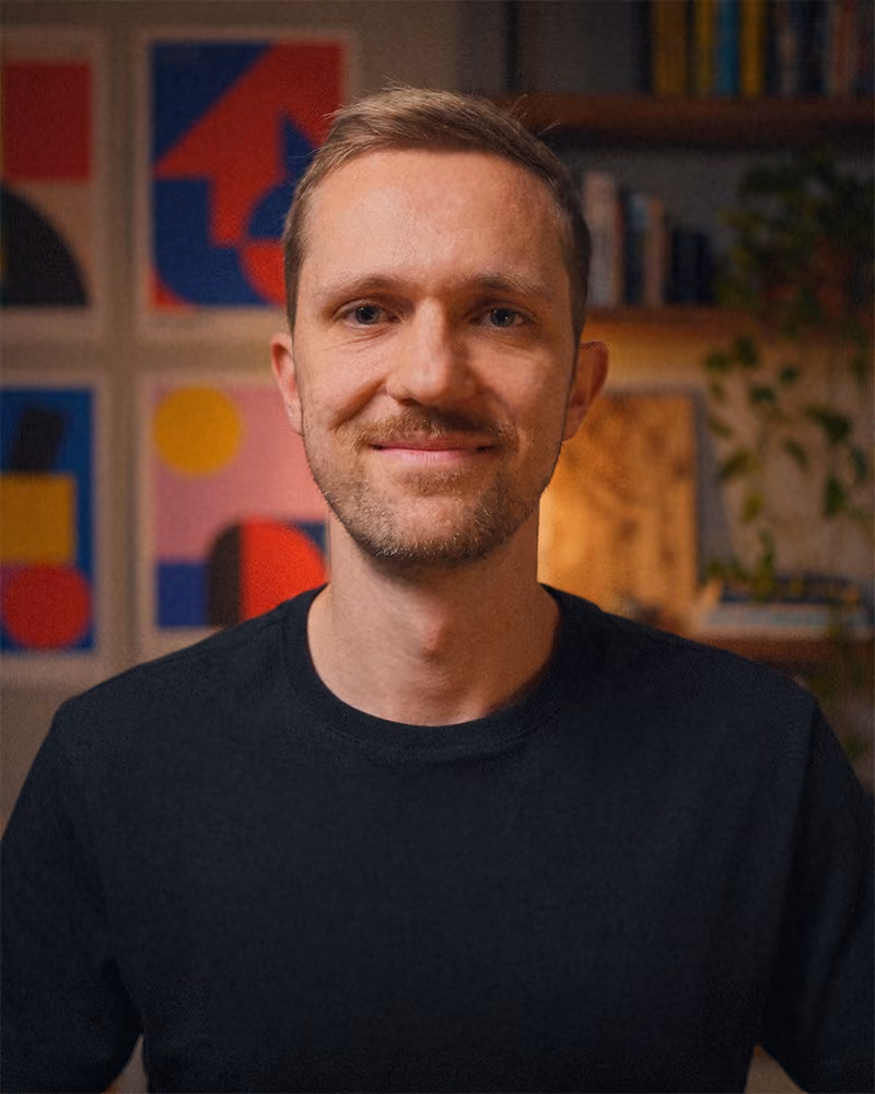 Smiling man with short hair and beard wearing a black shirt, colorful abstract art in background.