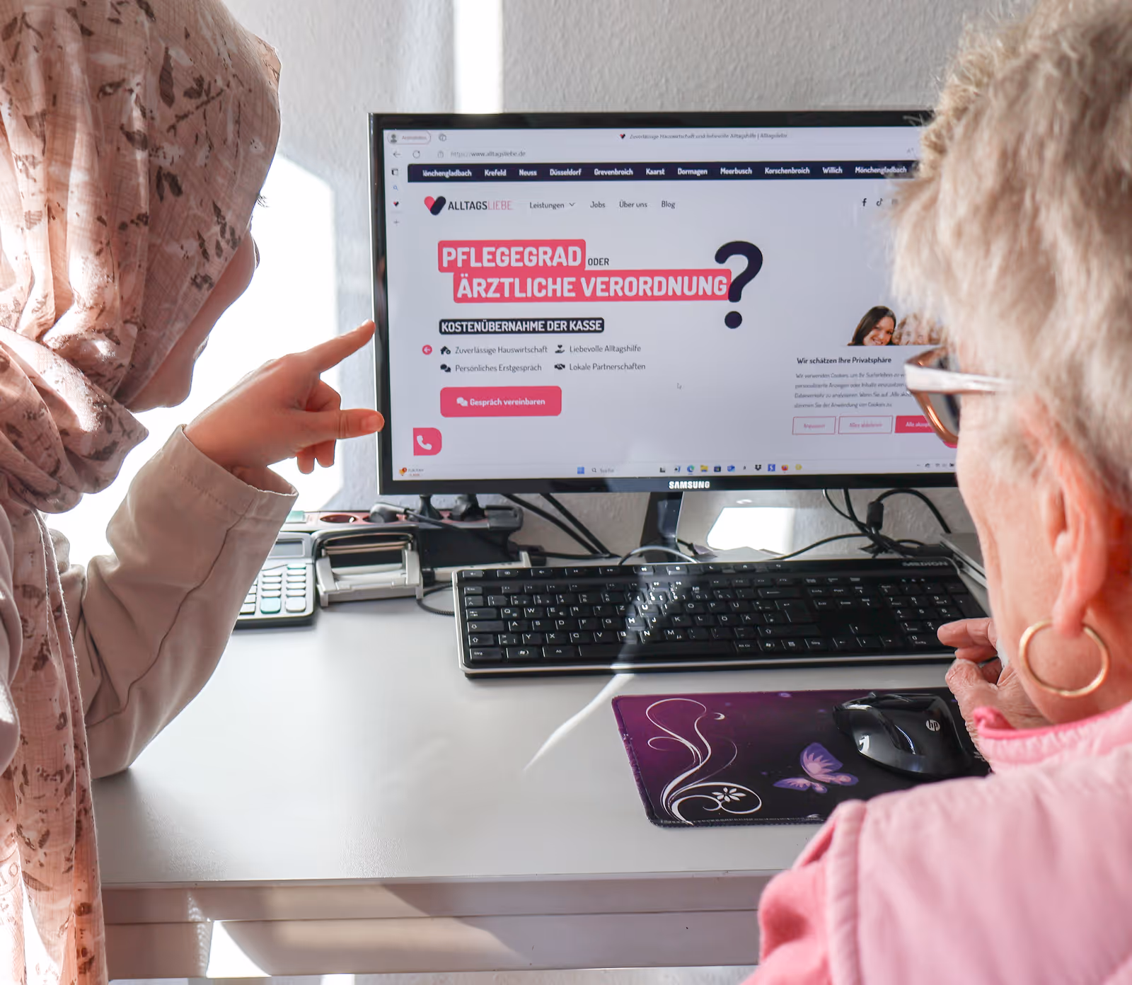 Alltagsbegleiterin erklärt älterer Frau am Computer die Online-Infos zu Pflegegrad und ärztlicher Verordnung