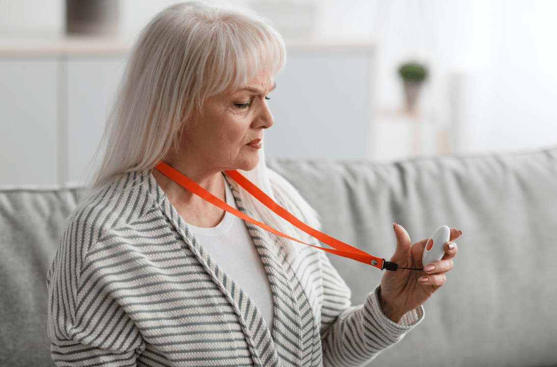 Seniorin drückt ihren Hausnotrufknopf mit rotem Band in der Hand - finanziert über die Pflegekasse