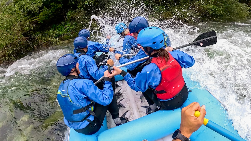 a blue raft enters a rapid sideways causing a big splash over the rafters in the boat