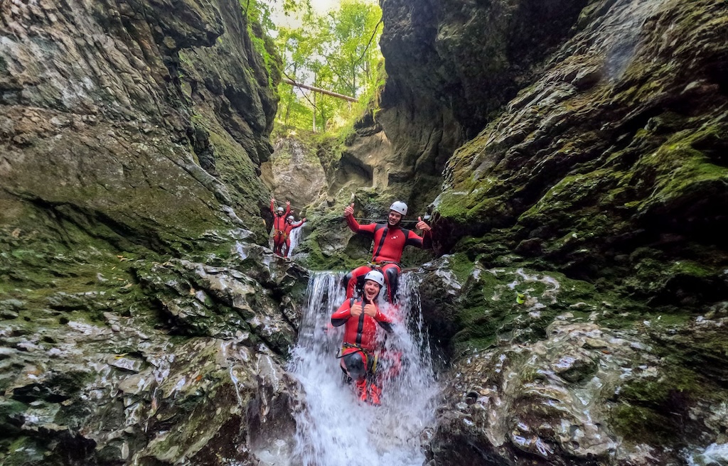 a group of friends sit in a small waterfall in a canyon in bled slovenia