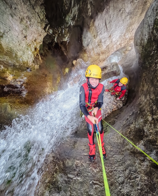 young boy rappels next to a waterfall in a narrow canyon