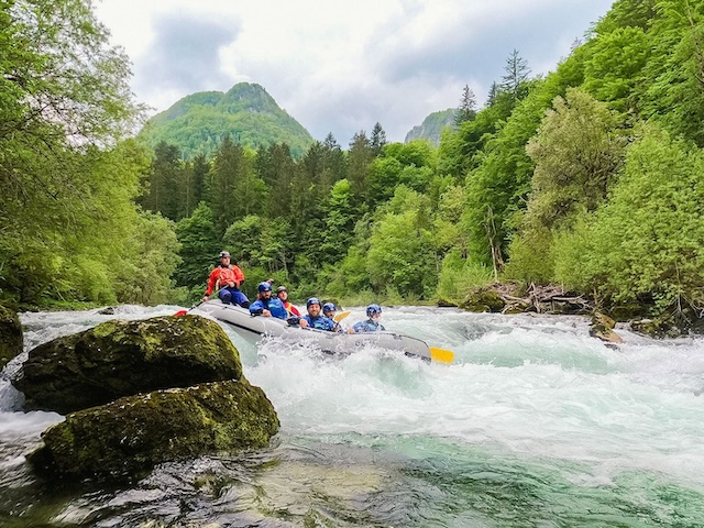 a raft descends down a rapid on the sava bohinjka river in slovenia surrounded by green trees and bush