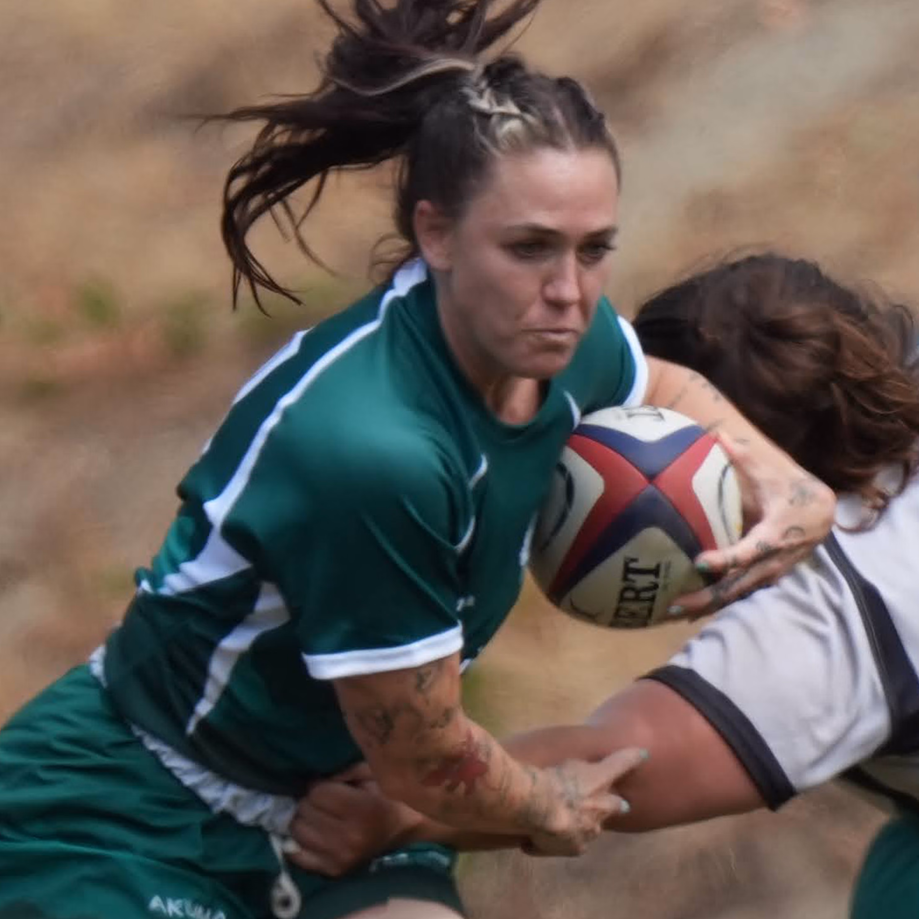 Female rugby player in white running with ball as opponents in dark kits try to tackle her.