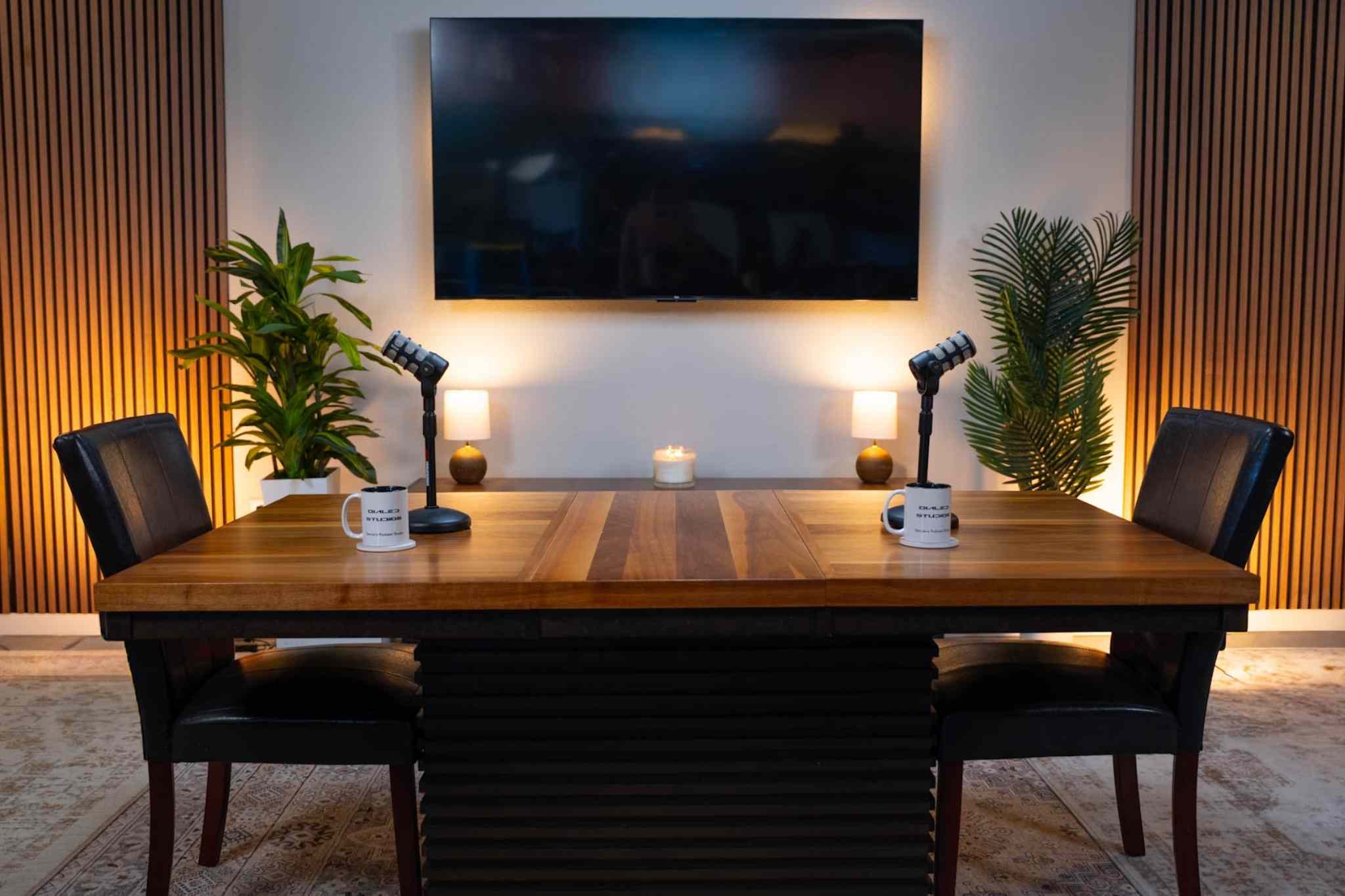 The Icon set at Dialed Studios, with a wood table, two chairs, microphones and a screen behind