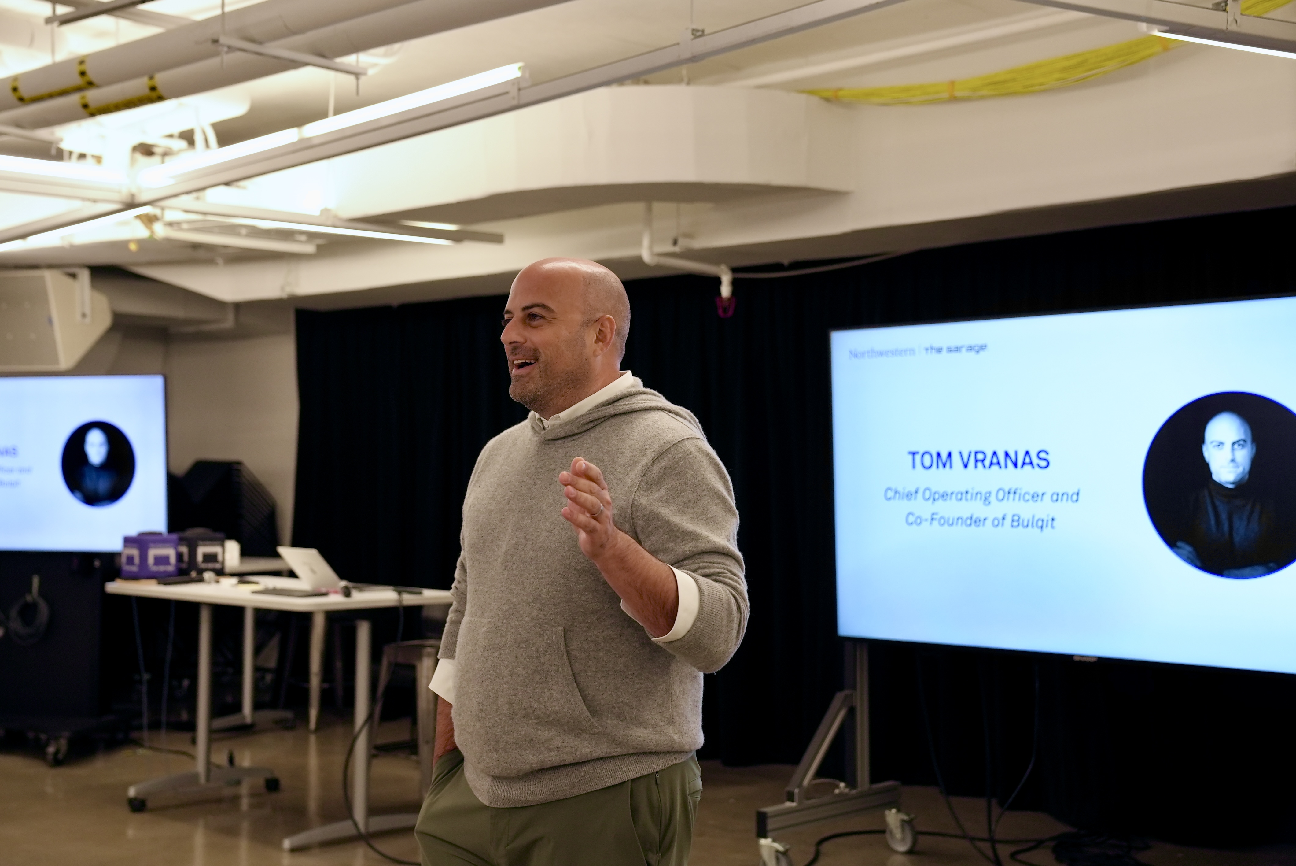 Tom Vranas stands at the front of the room presenting. 