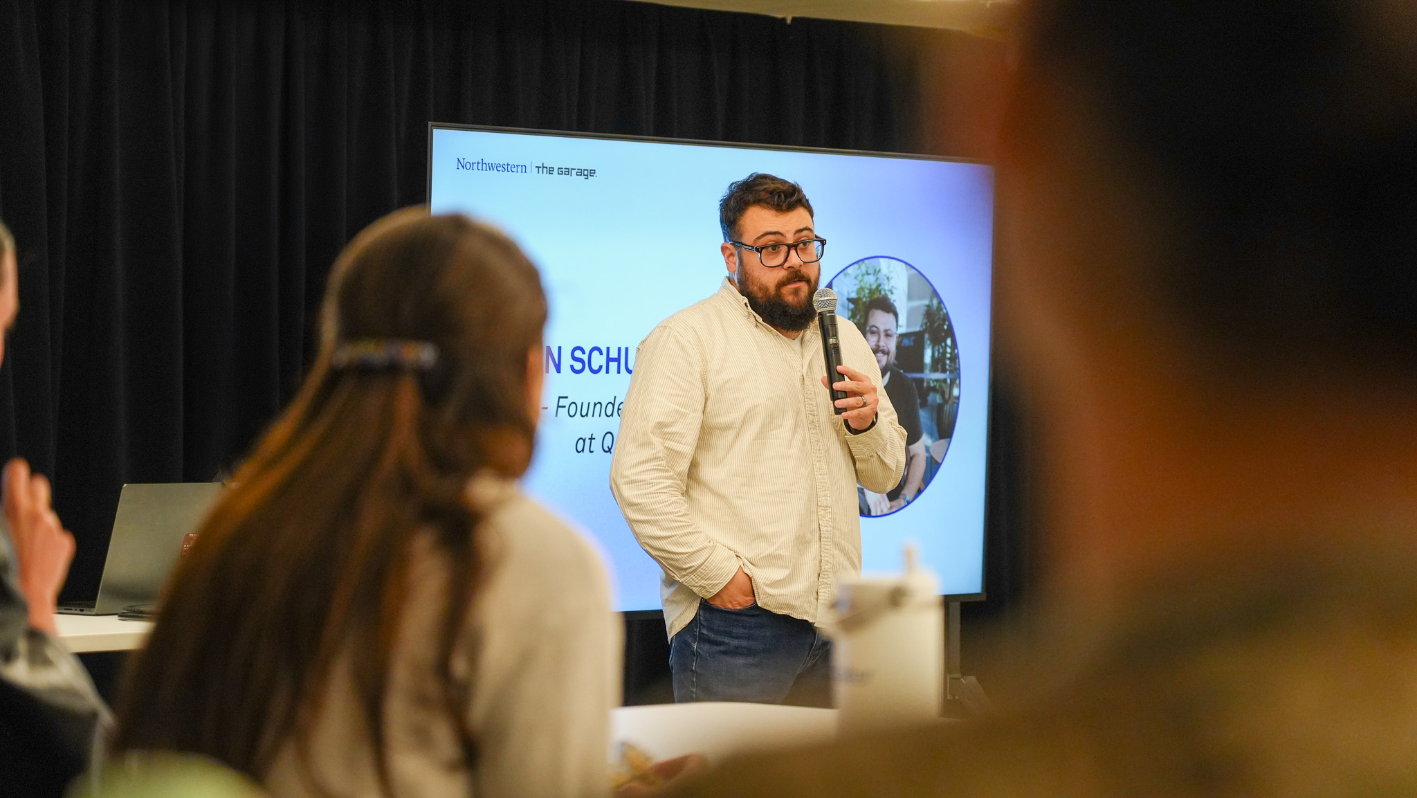 Dan stands at the front of the room holding a microphone.
