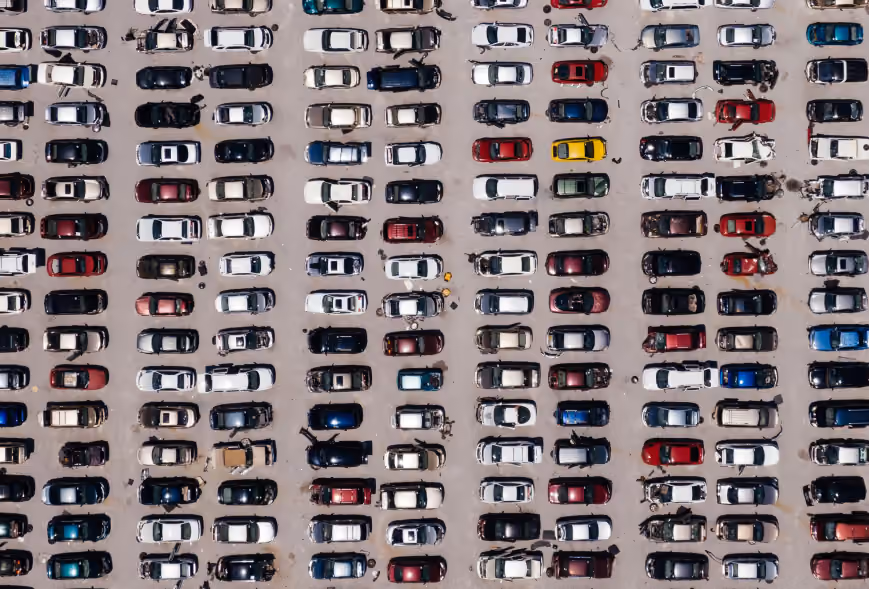 Aerial view of a packed auto salvage yard with rows of damaged cars on gray gravel