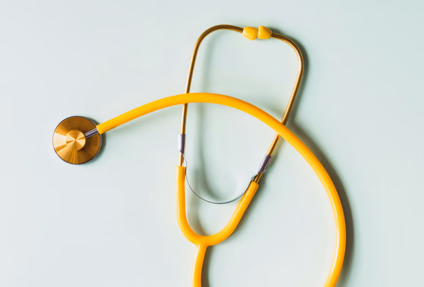 Yellow stethoscope with brass fittings arranged on a pale mint studio background