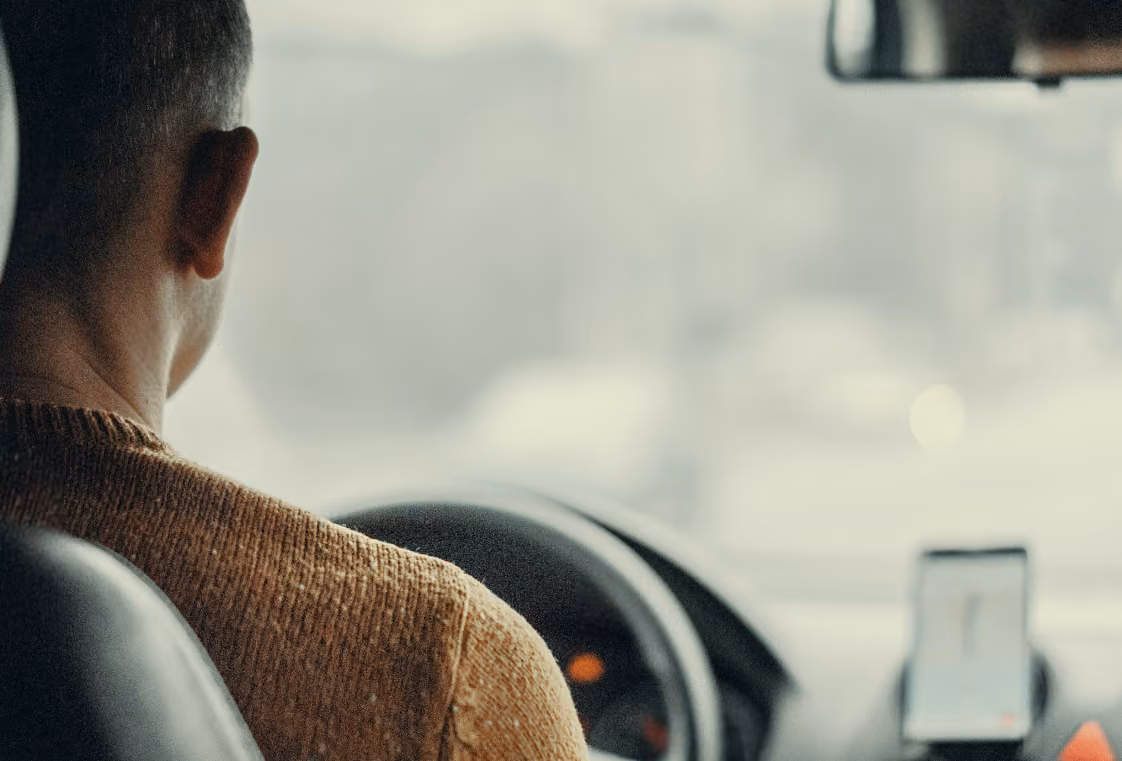 View from the back seat toward a driver and a phone showing a map mounted on the dashboard