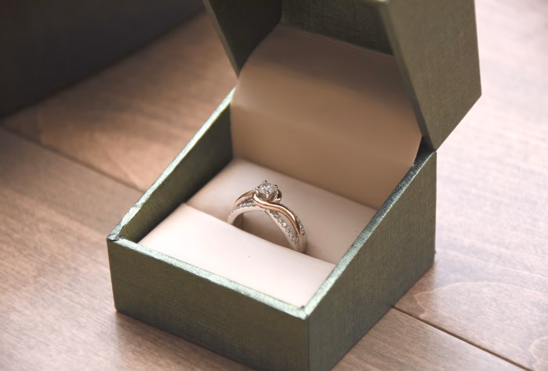 Diamond engagement ring displayed in an open dark green jewelry box on wood
