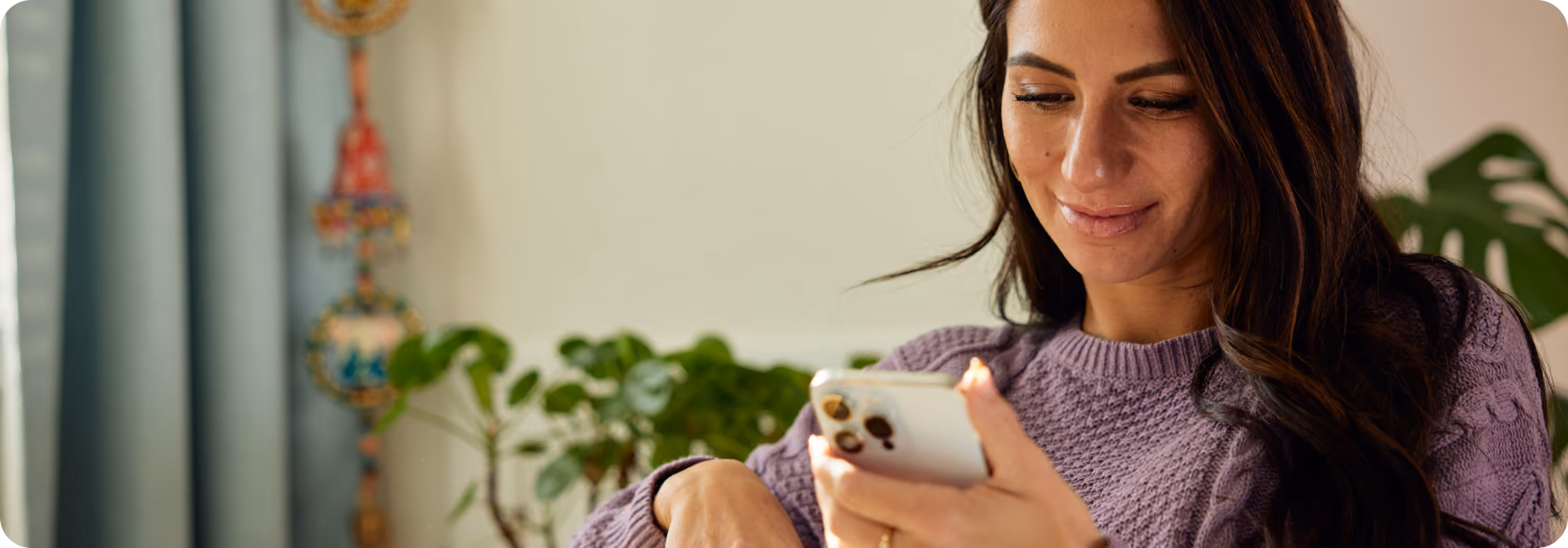 Woman in a purple sweater smiling while checking a smartphone near indoor plants