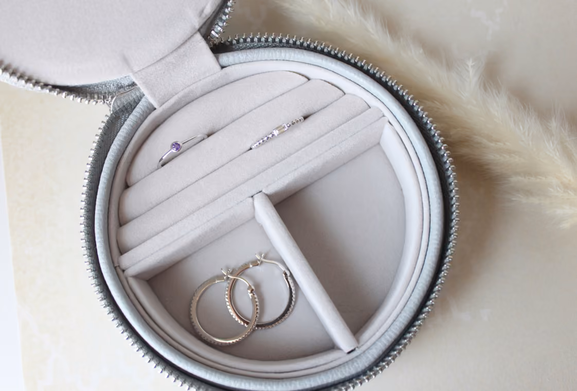 Open round gray travel jewelry case with rings and hoop earrings beside pampas grass