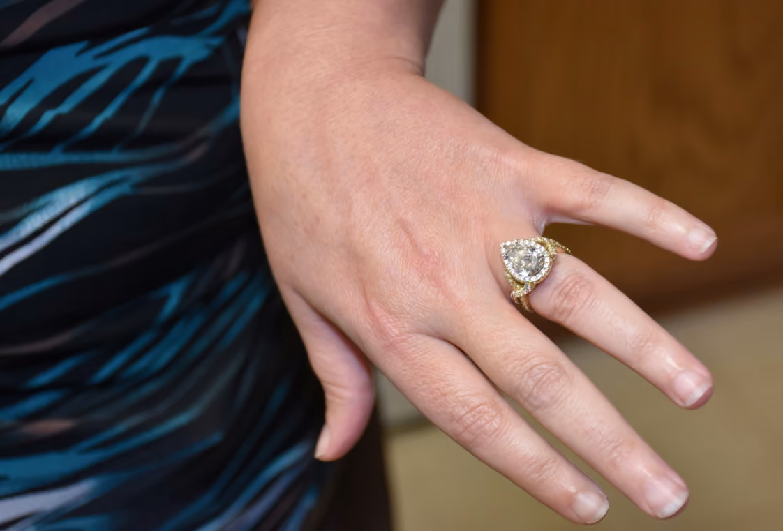 Close-up of a pear-shaped diamond halo engagement ring on a ring finger