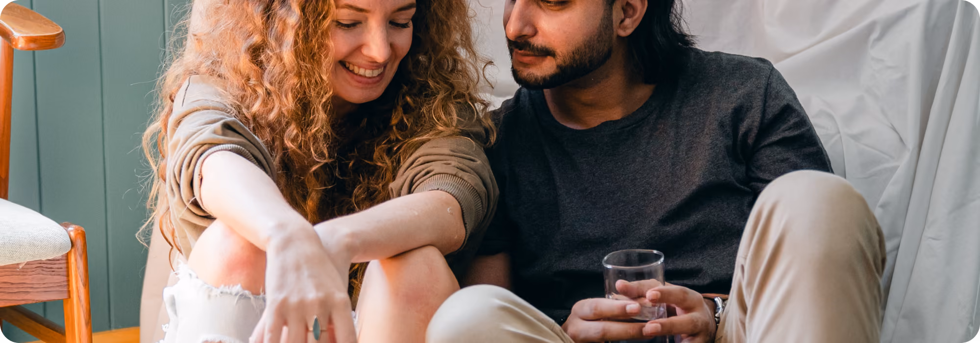 Young couple smiling while sitting close on the floor in a cozy softly lit living space