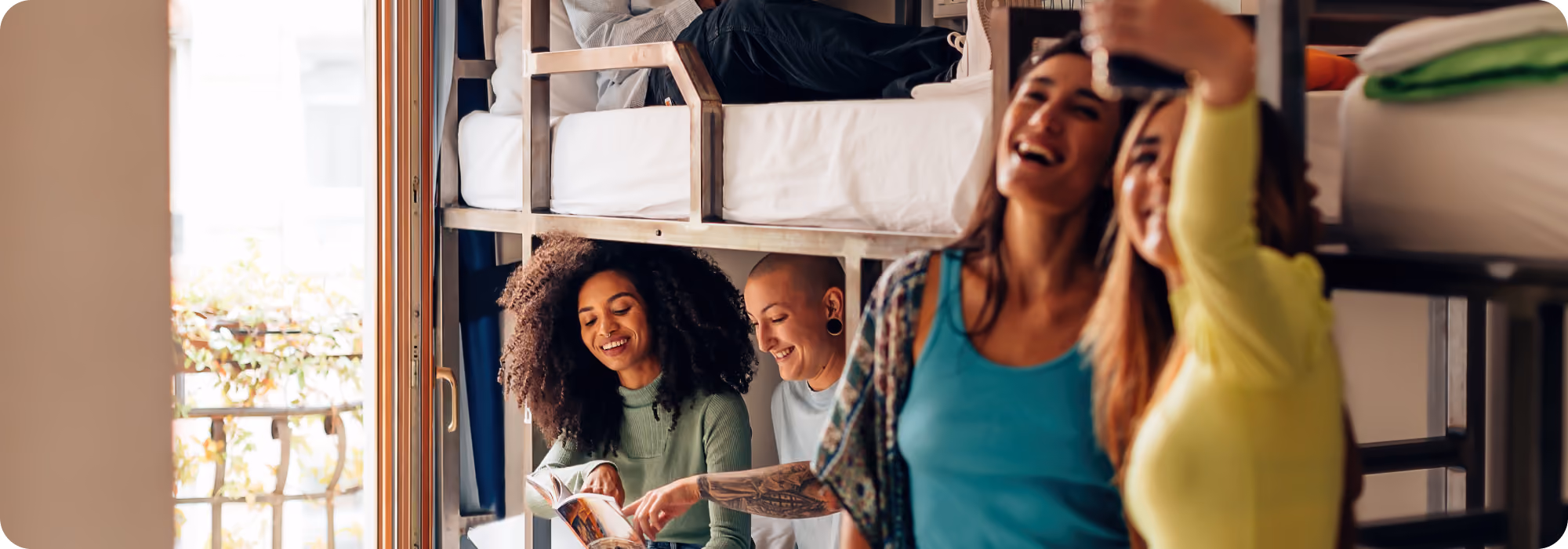 Friends socializing and taking photos in a bright hostel-style room with bunk beds