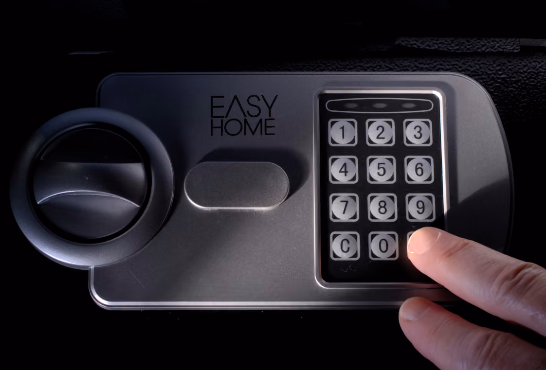 Finger pressing a glowing button on a small grey digital keypad safe