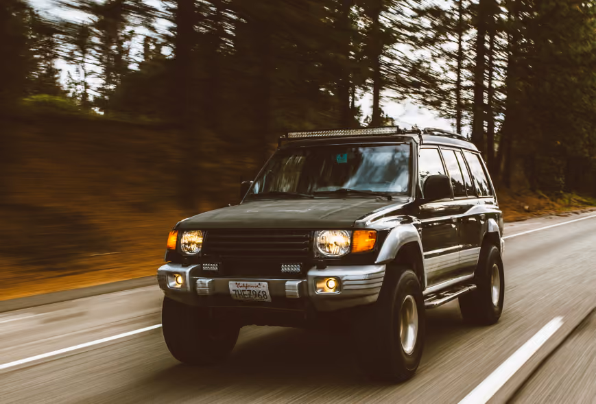 Lifted SUV with roof light bar driving fast on a forest-lined road with motion blur