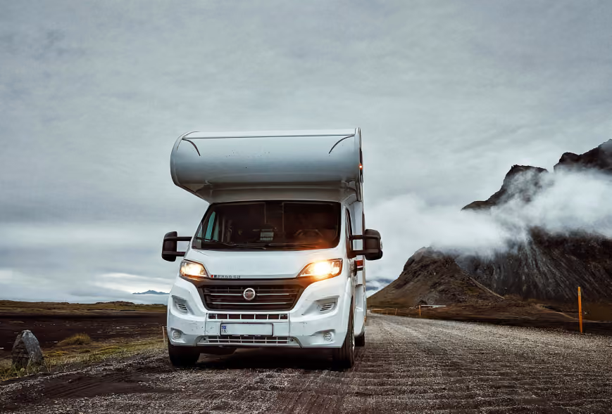 White motorhome facing the camera on a gravel road with misty mountains under heavy clouds