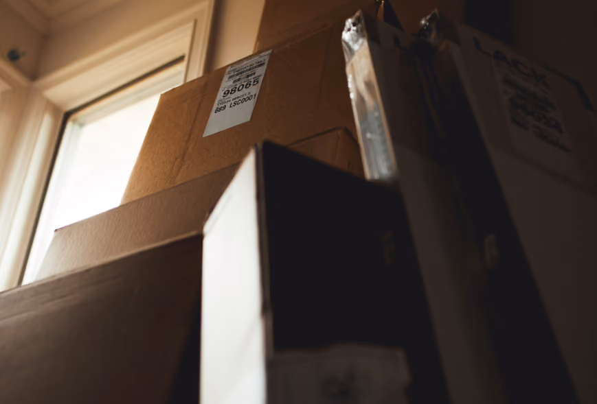 Stacked moving and flat-pack furniture boxes beside a sunlit apartment window