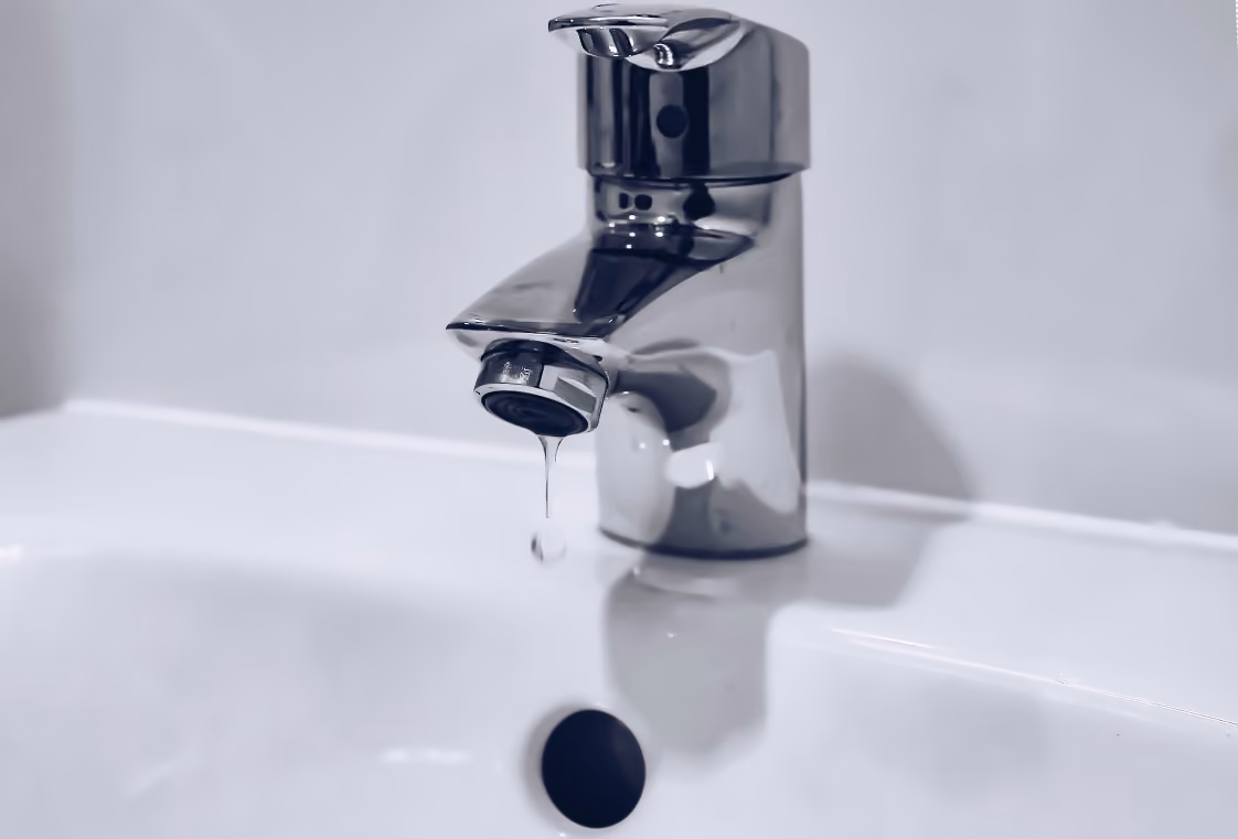 Chrome faucet dripping into a white basin sink with soft reflections