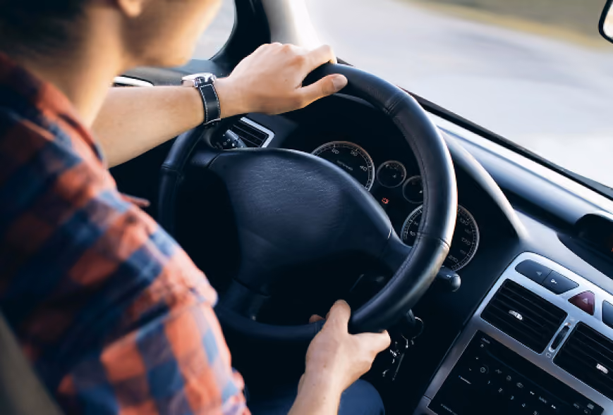 Driver in a plaid shirt holding a leather steering wheel with gauges and road blur ahead