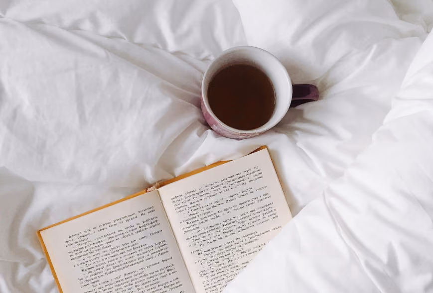 Purple mug and open hardcover book nestled in rumpled white bedding
