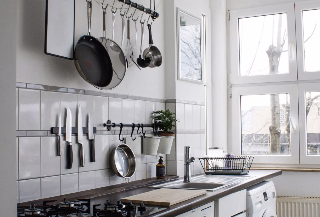 Organized kitchen wall with magnetic knife strip, hanging cookware, and sunlit windows