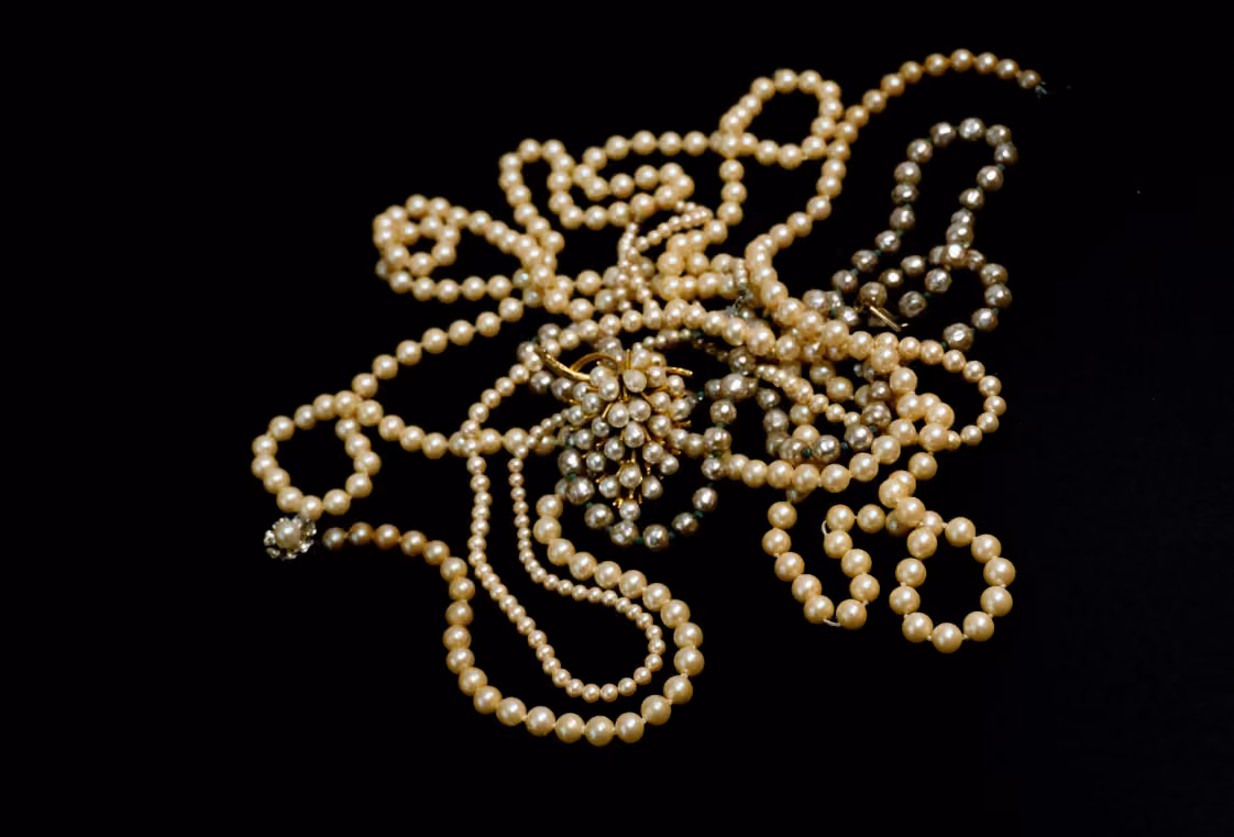 Tangled strands of cream and grey pearls and a round pearl cluster brooch on a black background